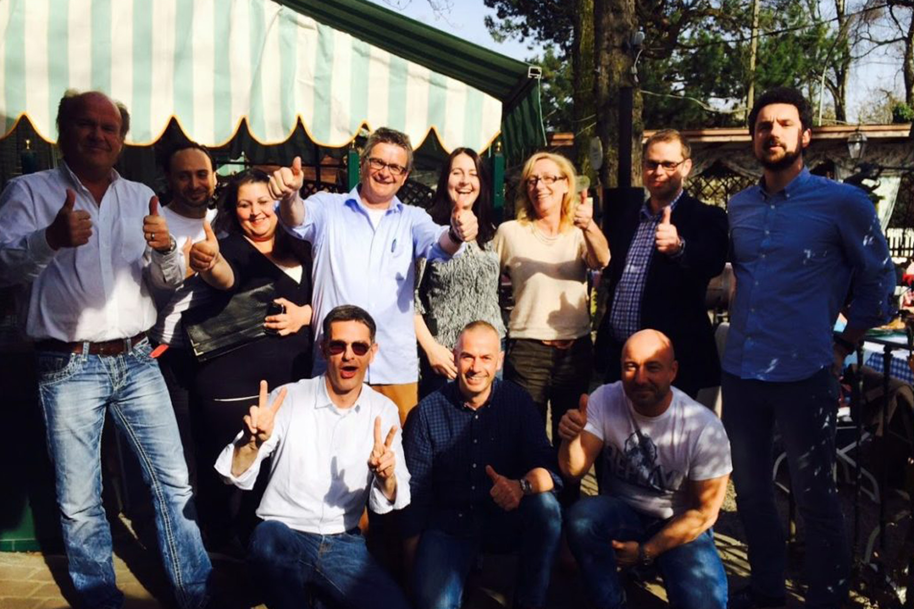 Fröhliche Gruppe von HappyMaids Franchisepartnern bei einem Partnertreffen im Freien, lächelnd und Daumen hoch