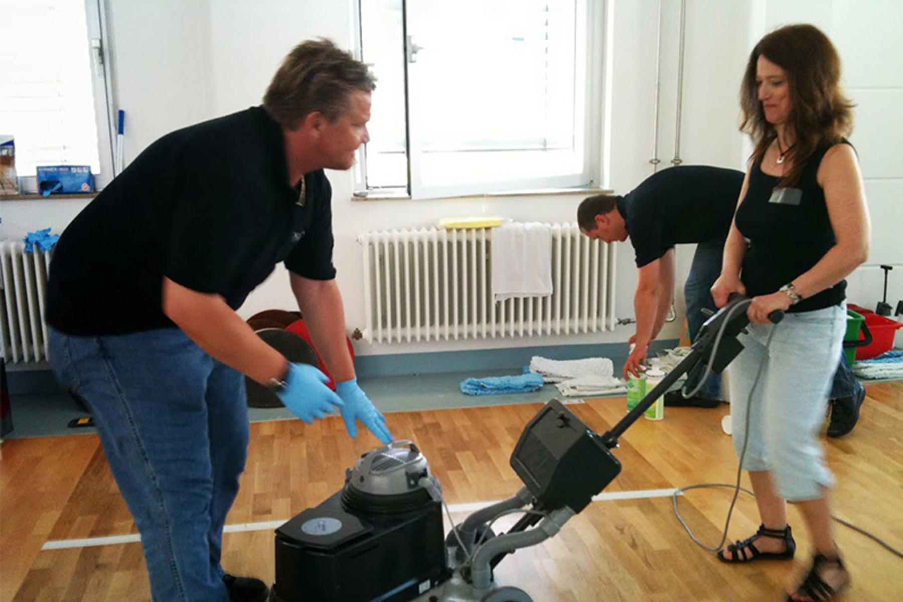 Drei HappyMaids Franchisepartner bei Praxisschulung: Reinigungsteam übt Bodenreinigung mit Poliermaschine in Seminarraum