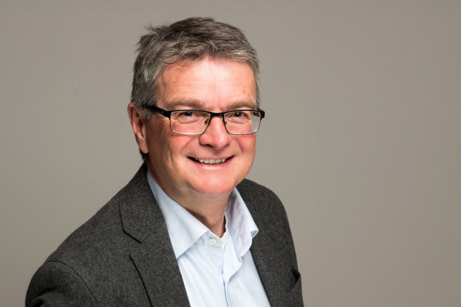 Porträt eines lächelnden Mannes mit Brille im Sakko vor neutralem Hintergrund, Business-Portrait für HappyMaids Helmut Schmid