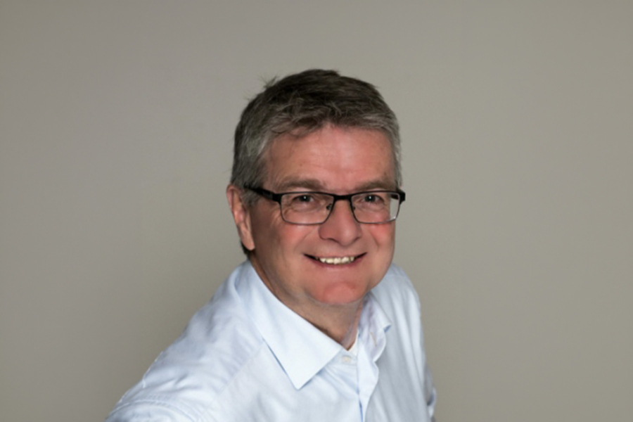Porträt eines lächelnden Mannes mit Brille in weißem Hemd vor neutralem Hintergrund, Firmenkontext HappyMaids Helmut Schmid