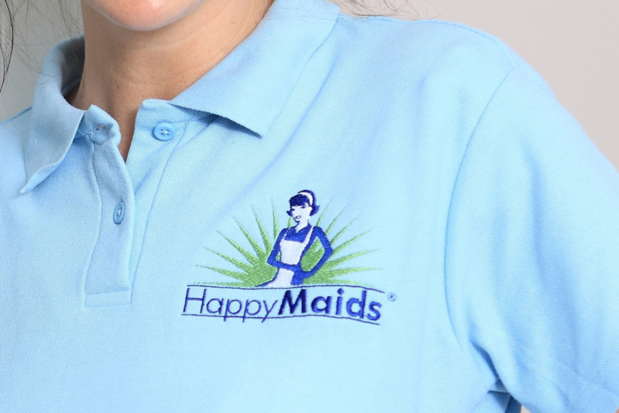 Nahaufnahme eines hellblauen Poloshirts mit gesticktem HappyMaids-Logo auf der Brust