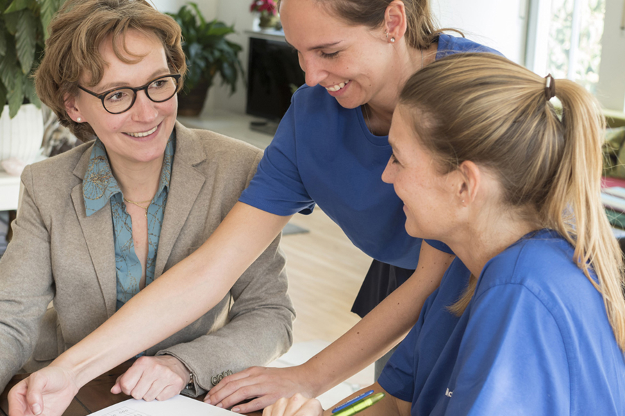 Drei HappyMaids Mitarbeiter bei Besprechung des Putzplans, lachend und gemeinsam am Tisch