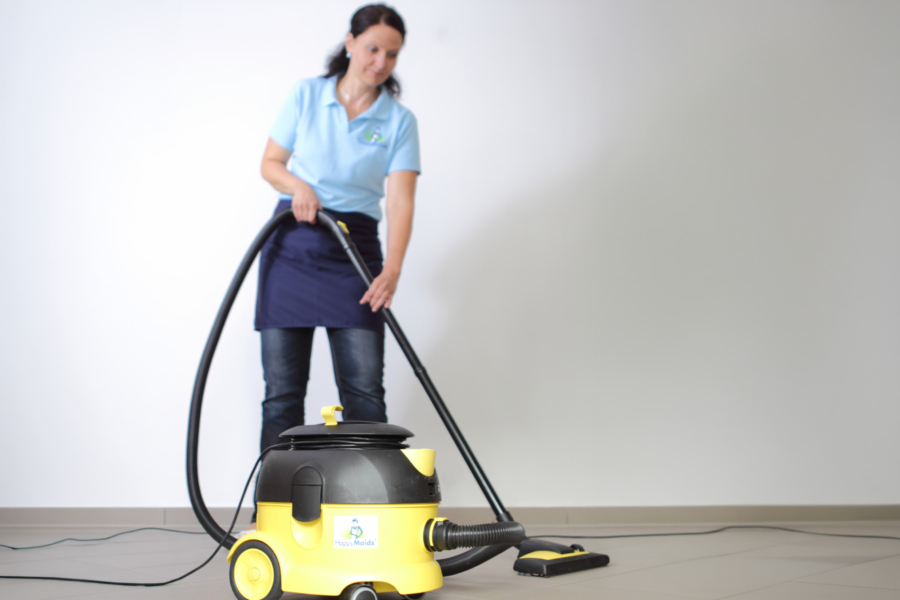 HappyMaids Mitarbeiterin beim Staubsaugen mit gelb-schwarzem Industrie-Staubsauger in heller Innenraum-Szene