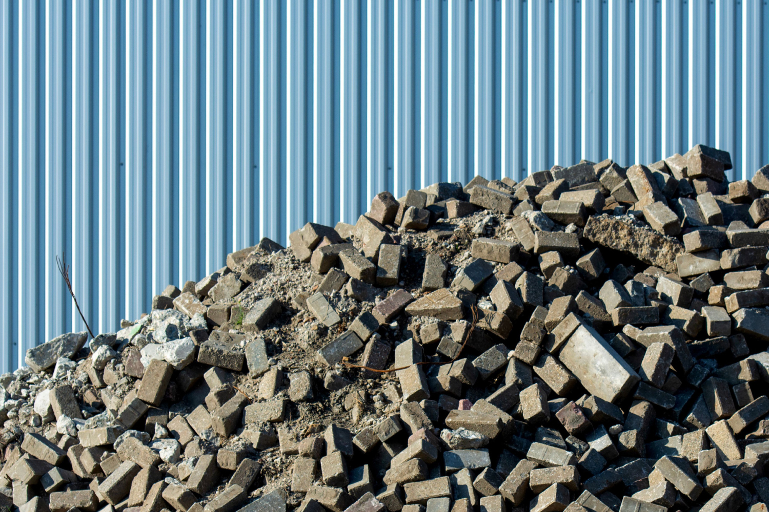 Haufen Bauschutt und Pflastersteine vor einer blauen Wellblechwand auf einer Baustelle