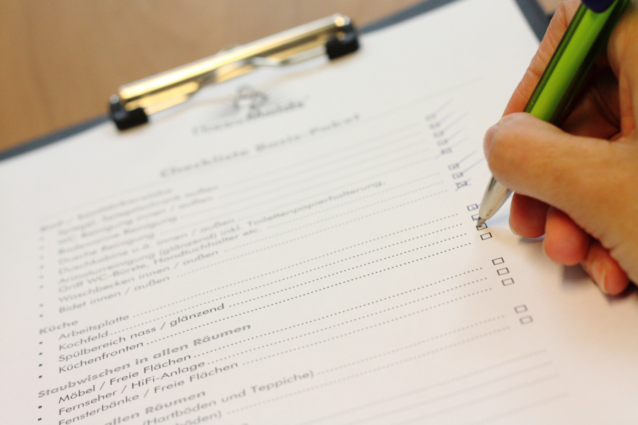 Hand setzt Häkchen auf HappyMaids Putzplan Checkliste auf Klemmbrett mit Stift