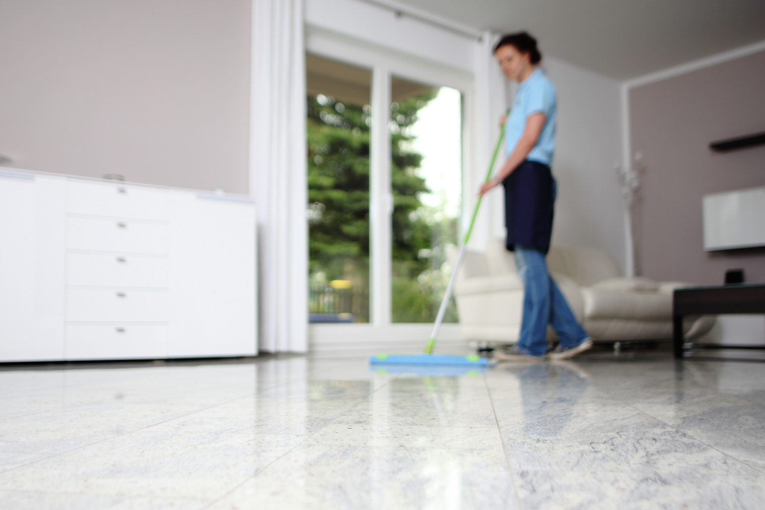 HappyMaids Reinigungskraft wischt glänzenden Marmorboden in modernem Wohnzimmer mit Fenstertür