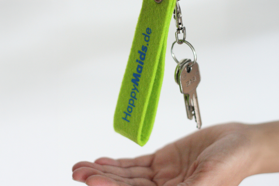 Hand übergibt Schlüssel mit grünem HappyMaids Schlüsselanhänger bei Schlüsselübergabe