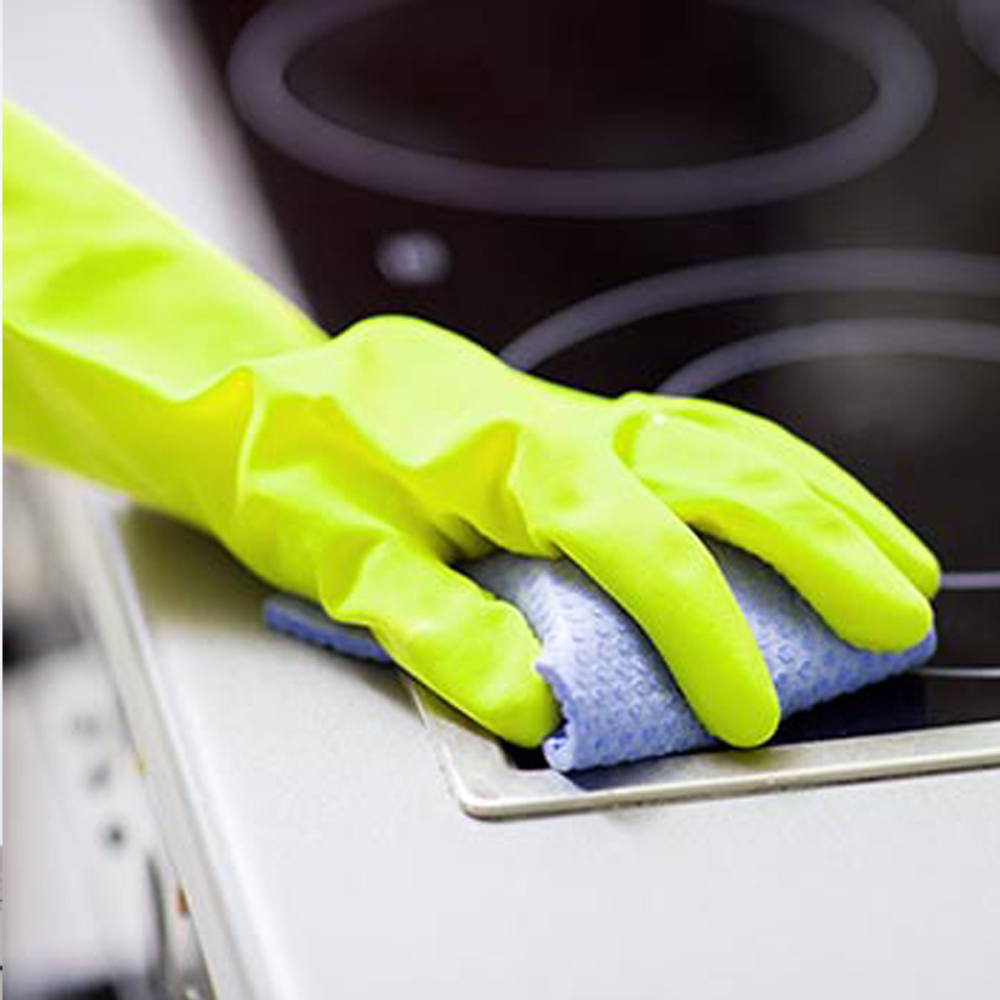 Hand mit gelbem Putzhandschuh wischt Kochfeld mit Mikrofaser-Tuch – HappyMaids Vorteile Hygieneanspruch
