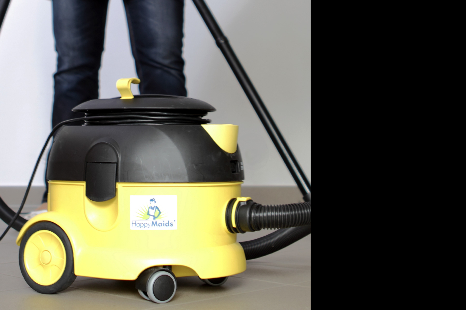 Gelber Profi-Nasssauger mit HappyMaids-Logo und Schlauch vor Person in Jeans, professionelle Ausrüstung für Reinigung